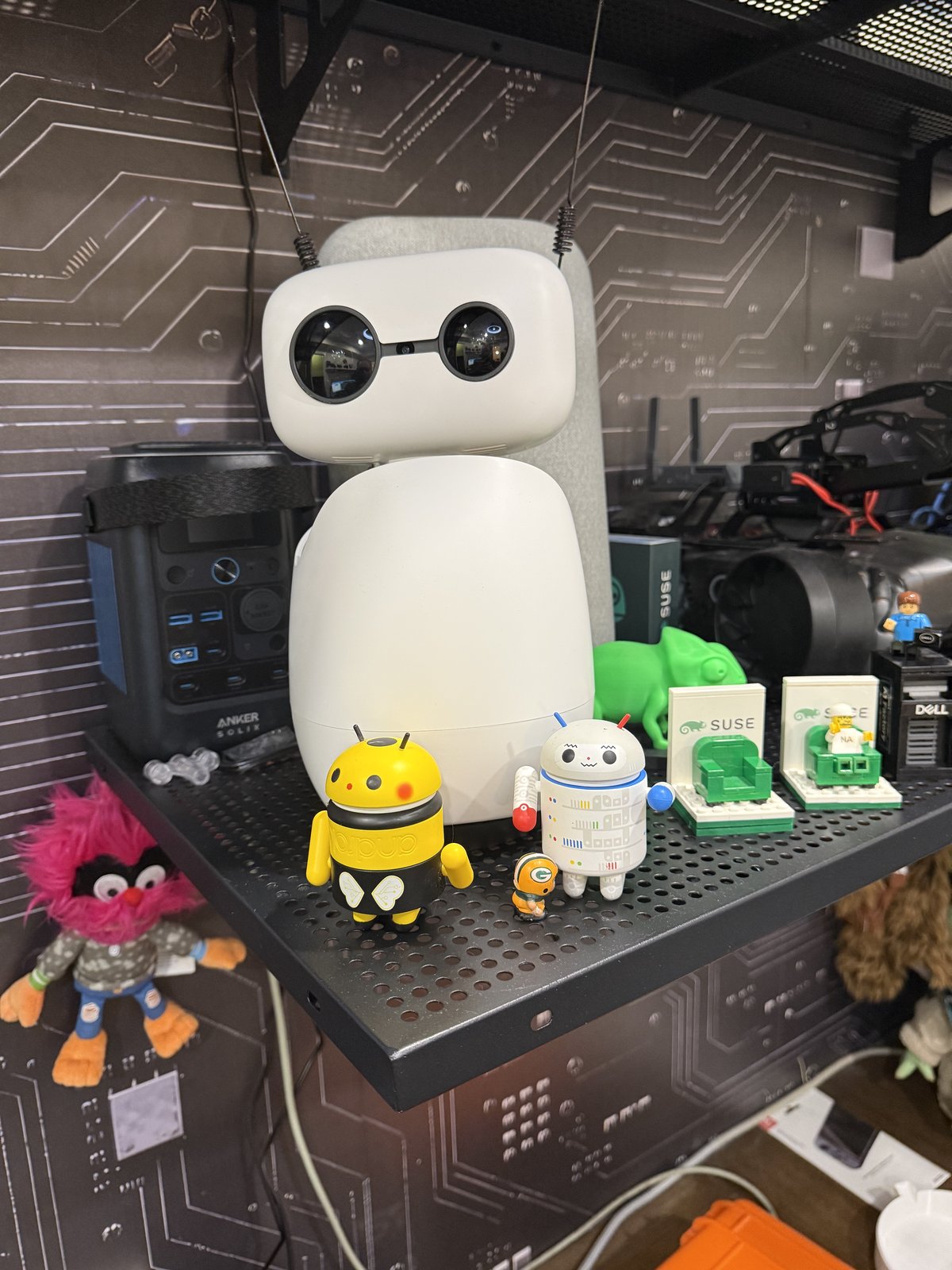Reachy Mini, a white robot with round glasses-like eyes and two antennas, on a shelf among lab gear